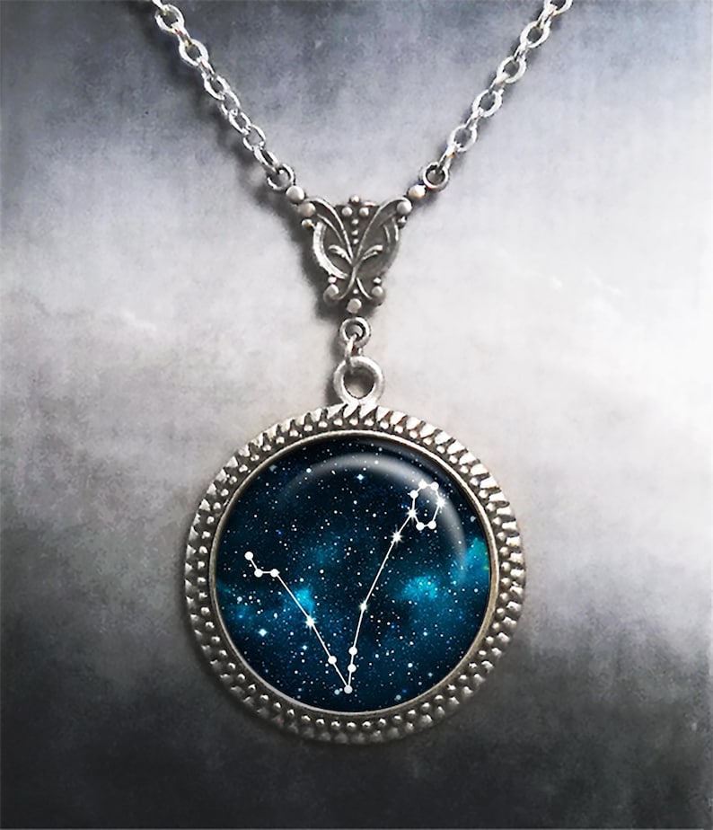 K&ouml;nnte beinhalten: Eine silberne Halskette mit einem runden Anh&auml;nger, der einen blauen Galaxie-Hintergrund mit wei&szlig;en Sternen zeigt, die die Konstellation Fische bilden.