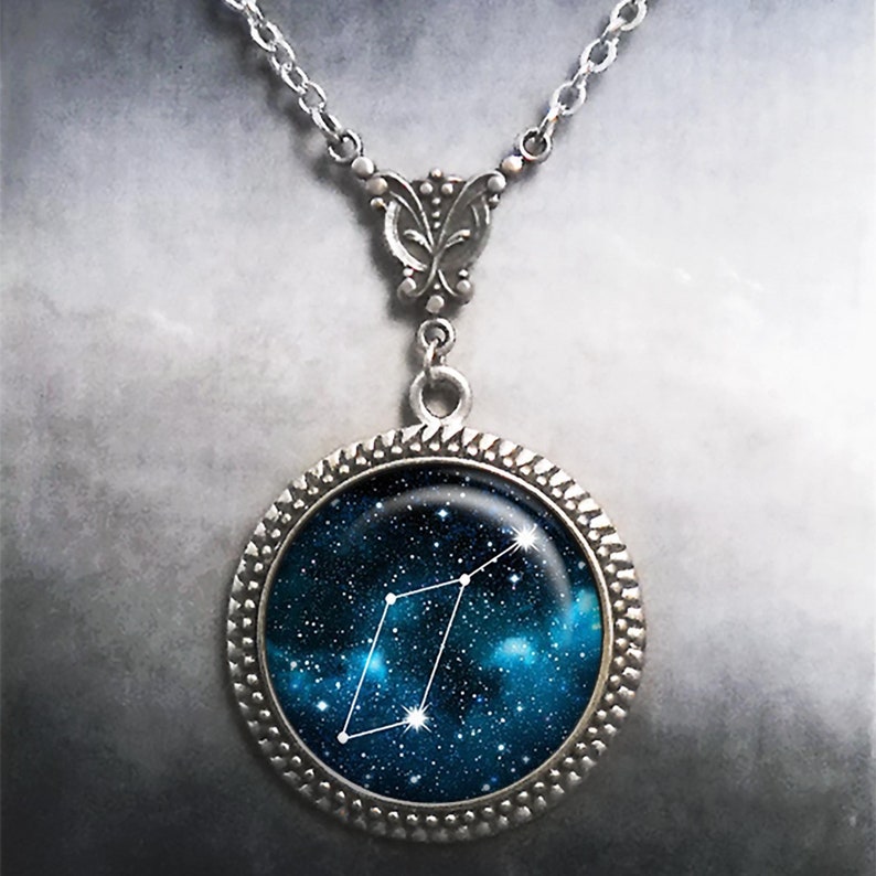 May include: A silver necklace with a round pendant featuring a constellation against a blue and black galaxy background.