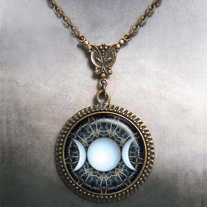 May include: A bronze necklace with a round pendant featuring a triple moon symbol in white on a blue and gold background. The pendant is surrounded by a decorative bronze frame.