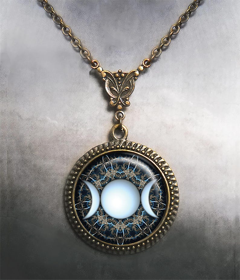 May include: A bronze necklace with a round pendant featuring a triple moon symbol in white on a blue and gold background. The pendant is surrounded by a decorative bronze frame.
