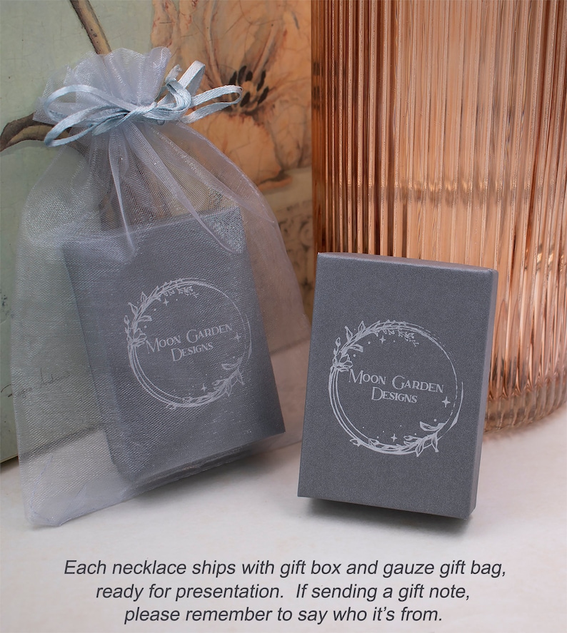 May include: A gray gift box with a white floral design and the text "Moon Garden Designs". The box is sitting on a white gauze bag.