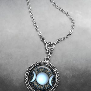 May include: A silver chain necklace with a round pendant featuring a triple moon symbol in white on a blue and gold background.