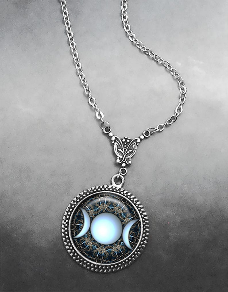 May include: A silver chain necklace with a round pendant featuring a triple moon symbol in white on a blue and gold background.