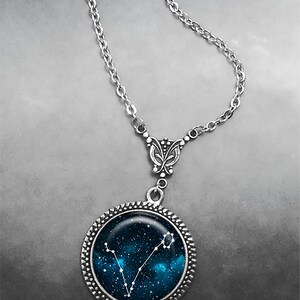 K&ouml;nnte beinhalten: Eine silberne Kettenkette mit einem silbernen Anh&auml;nger mit einem blauen und wei&szlig;en Glascabochon mit einem Konstellationsdesign. Die Konstellation ist Fische.