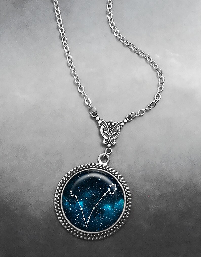 K&ouml;nnte beinhalten: Eine silberne Kettenkette mit einem silbernen Anh&auml;nger mit einem blauen und wei&szlig;en Glascabochon mit einem Konstellationsdesign. Die Konstellation ist Fische.