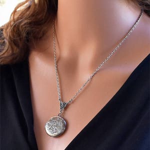 May include: A silver locket necklace with a delicate chain and a floral design on the locket.