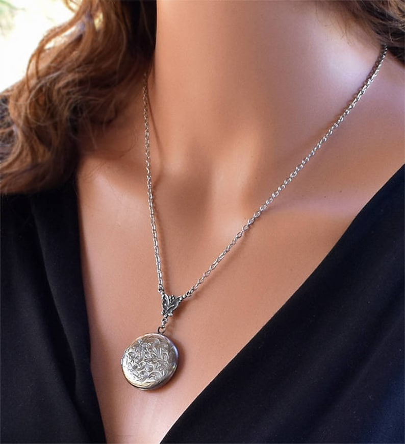 May include: A silver locket necklace with a delicate chain and a floral design on the locket.