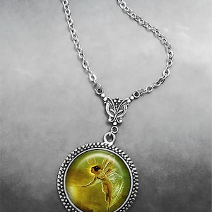 May include: A silver necklace with a round pendant featuring a painting of a fairy with wings, holding a glowing orb. The pendant has a silver filigree border and a silver butterfly charm.