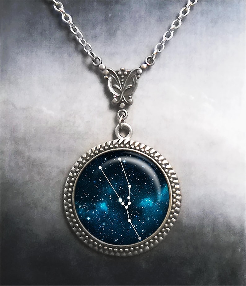 May include: A silver necklace with a round pendant featuring a blue galaxy background with white stars and the constellation Taurus.