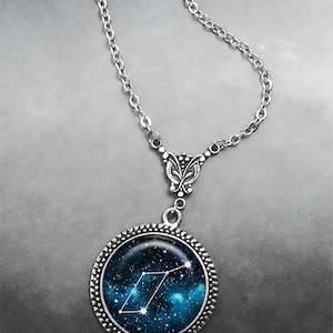 May include: A silver chain necklace with a round pendant featuring a blue and black galaxy print with a white constellation design.