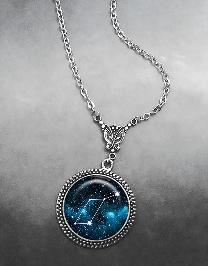 May include: A silver chain necklace with a round pendant featuring a blue and black galaxy print with a white constellation design.