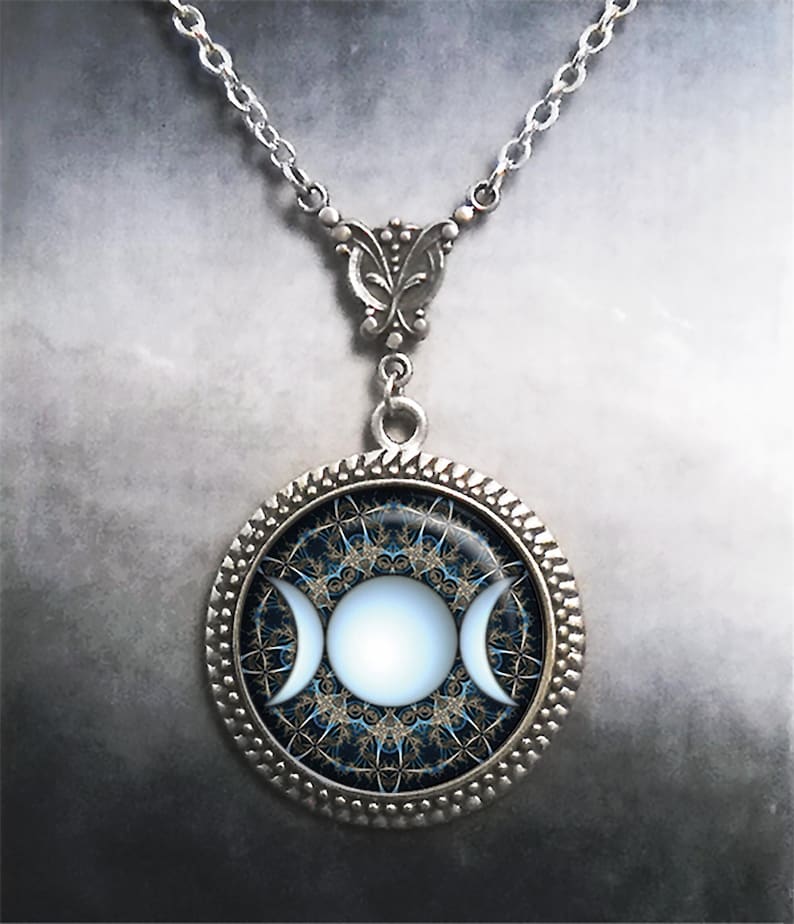 May include: A silver necklace with a round pendant featuring a triple moon symbol in white against a blue and gold background.