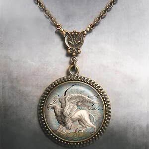 May include: A bronze necklace with a round pendant featuring a vintage illustration of a griffin. The pendant has a glass cover and a decorative border. The necklace has a butterfly-shaped clasp.