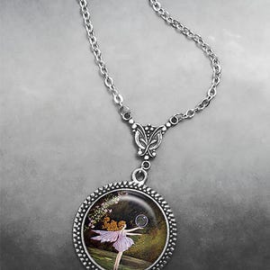 May include: Silver necklace with a circular pendant showing a fairy illustration. The pendant has a beaded border and a chain with a butterfly-shaped connector. The fairy is in a purple dress, with a bubble in front of her.