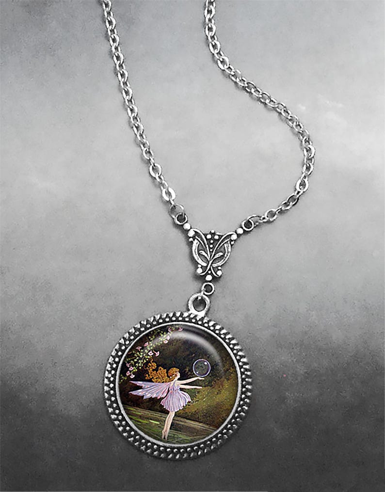 May include: Silver necklace with a circular pendant showing a fairy illustration. The pendant has a beaded border and a chain with a butterfly-shaped connector. The fairy is in a purple dress, with a bubble in front of her.