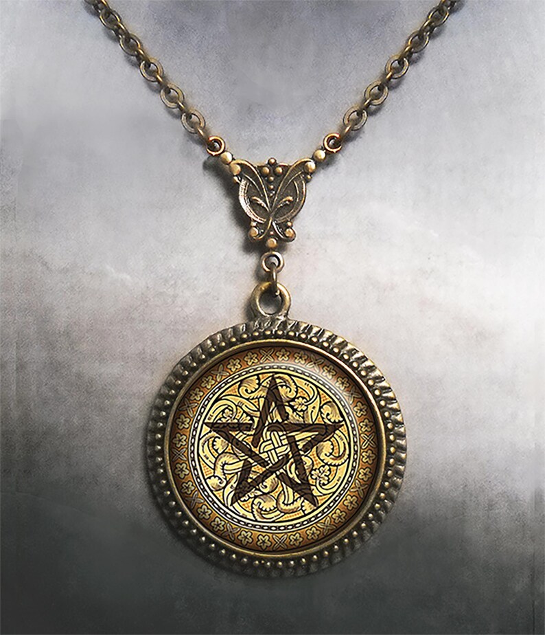 May include: A round pendant necklace featuring an antique bronze-toned metal frame with a textured edge. The center displays a dark brown pentagram symbol set against a gold-colored background with intricate, swirling floral and vine patterns.