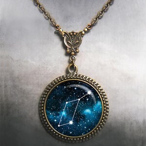 May include: A bronze necklace with a round pendant featuring a constellation against a blue galaxy background. The pendant has a decorative border.
