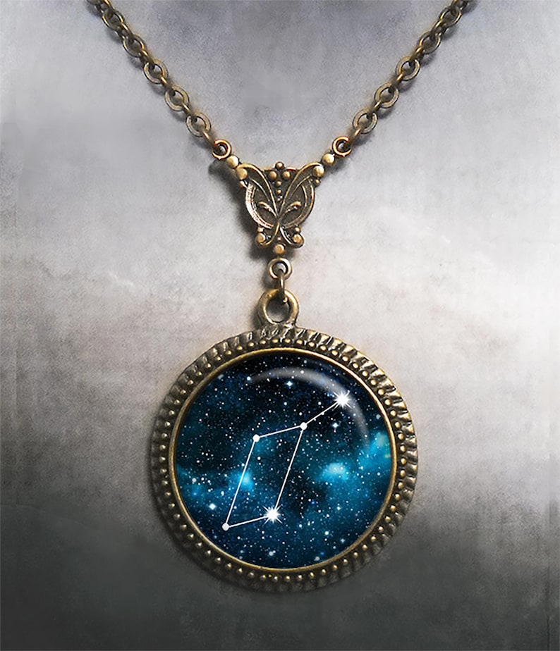 May include: A bronze necklace with a round pendant featuring a constellation against a blue galaxy background. The pendant has a decorative border.