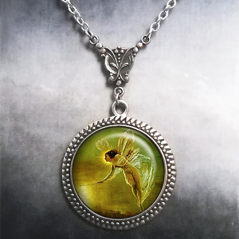 May include: A silver necklace with a round pendant featuring a vintage illustration of a fairy with wings, holding a wand, against a green and gold background.