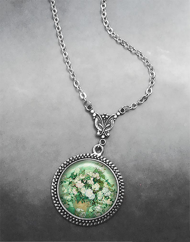 May include: A silver chain necklace with a round pendant featuring a painting of white flowers in a vase. The pendant has a silver frame with a beaded edge.