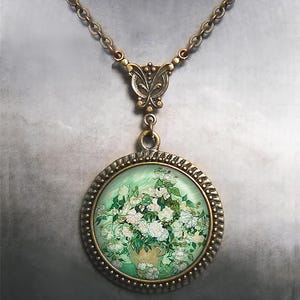 May include: A bronze necklace with a round pendant featuring a painting of white roses in a vase. The pendant has a decorative border and the chain has a butterfly clasp.
