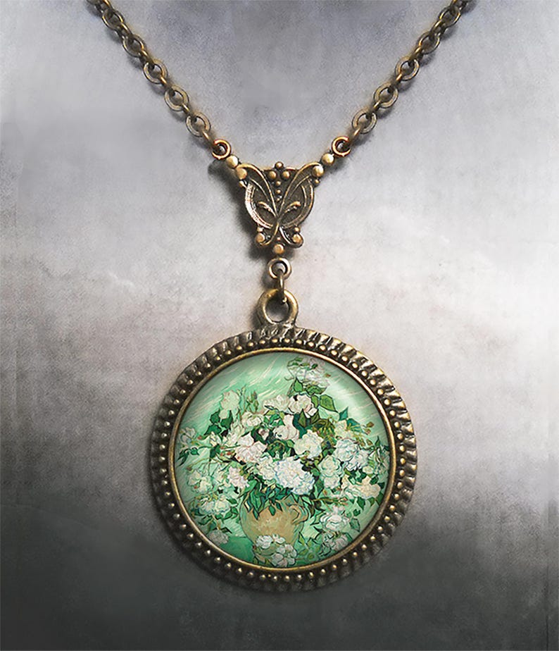 May include: A bronze necklace with a round pendant featuring a painting of white roses in a vase. The pendant has a decorative border and the chain has a butterfly clasp.