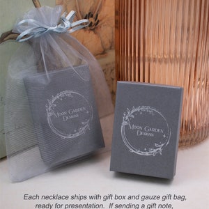 May include: A gray gift box with a white floral design and the text "Moon Garden Designs". The box is sitting on a white gauze bag.