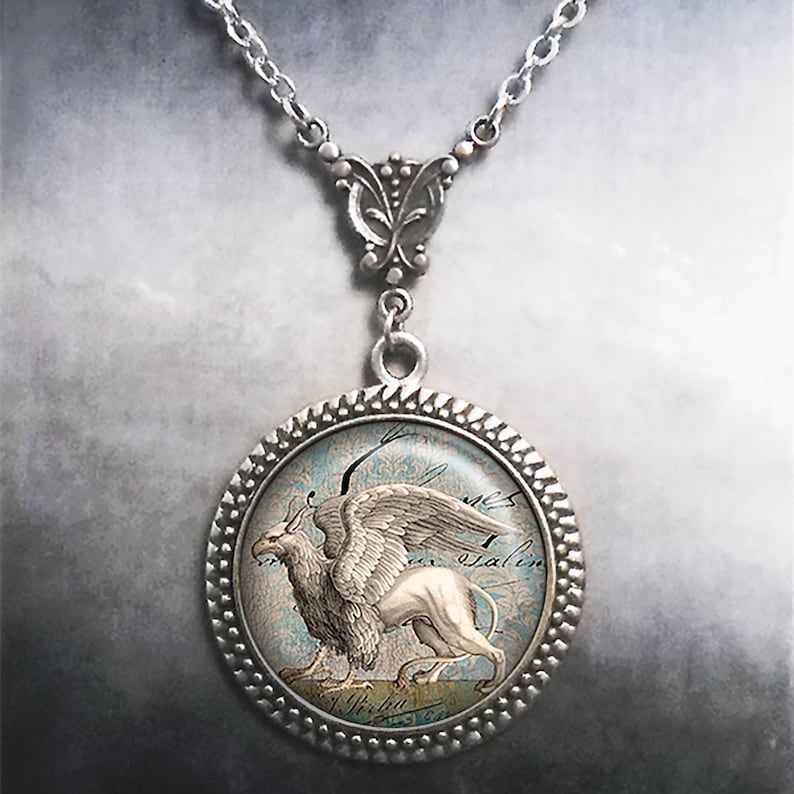 May include: Silver necklace with a round pendant featuring a vintage illustration of a griffin, a mythical creature with the head and wings of an eagle and the body of a lion. The pendant has a decorative silver frame.