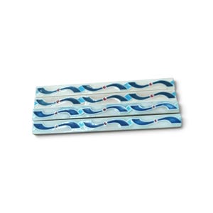 May include: Four rectangular ceramic tiles arranged in a stack. Each tile features a white base with a repeating pattern of dark blue and light blue wavy lines, accented by small, circular red dots placed at intervals along the design.