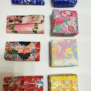 Puede incluir: Una colección de ocho artículos de tela pequeños, que incluye cuatro estuches rectangulares con cierre de broche y cuatro cajas cuadradas, todos con diversos patrones florales y geométricos coloridos en tonos azul, rosa, rojo y amarillo.