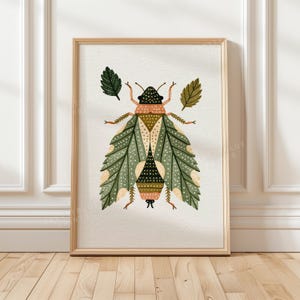 May include: A framed art print featuring a stylized insect with large, patterned green wings, a dark head, and a segmented body in shades of tan and brown. Two small, distinct leaves are positioned on either side of the insect's upper body.