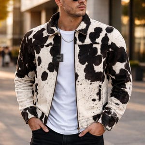 Könnte beinhalten: Jacke mit Kuhfellmuster mit schwarzen und weißen Flecken. Die Jacke hat einen Kragen, einen Reißverschluss und Taschen. Die Person trägt ein weißes T-Shirt und eine schwarze Jeans. Die Person trägt auch eine Sonnenbrille.