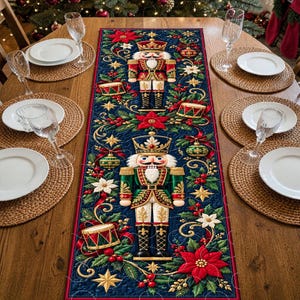 May include: A rectangular table runner featuring a dark blue background with two nutcracker figures, red poinsettias, green holly leaves, gold stars, and small drums. The runner is centered on a wooden table with white plates and clear glasses.