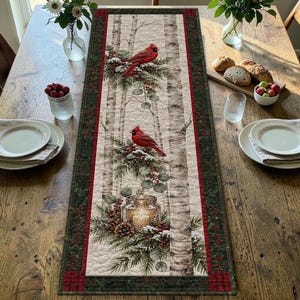 May include: A rectangular quilted table runner featuring a winter forest scene with white birch trees, two red cardinals perched on pine branches, and a lit candle in a glass jar. The runner has a dark green border with red berry accents.