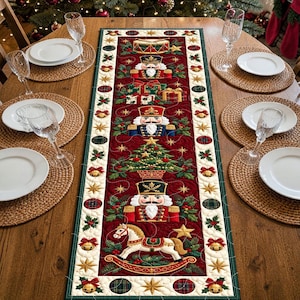 May include: A rectangular quilted table runner featuring a deep red background with a central vertical pattern of nutcrackers, a Christmas tree, a rocking horse, and wrapped gifts, bordered by a green trim with gold stars and bells.