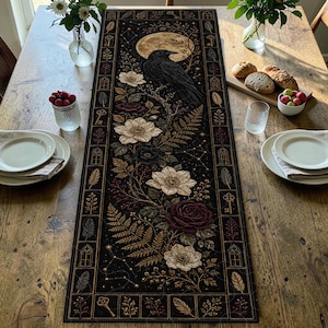 Puede incluir: Un camino de mesa rectangular negro con una ilustración central de un cuervo negro posado en una rama bajo una luna llena, rodeado de flores blancas y rojo oscuro, helechos, llaves y plumas dentro de un marco decorativo.