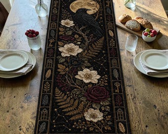 May include: A rectangular black table runner featuring a central illustration of a black raven perched on a branch under a full moon, surrounded by white and dark red flowers, ferns, keys, and feathers within a decorative border frame.