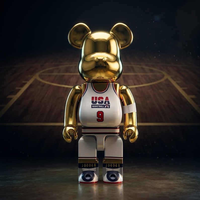 Pu&ograve; includere: Una statuetta da collezione a forma di orso color oro che indossa una canotta da basket bianca con la scritta USA BASKETBALL e il numero 9 sul davanti. La statuetta ha un polsino bianco sul braccio sinistro e scarpe bianche con dettagli neri e rossi.