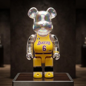 Pu&ograve; includere: Una statuetta da collezione a forma di orso con testa e arti trasparenti e iridescenti. Il busto presenta il design di una maglia da basket gialla dei Los Angeles Lakers con la scritta Lakers e il numero 6 in viola, oltre a un piccolo numero 6 sul petto.