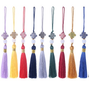 May include: A collection of colorful tassel ornaments. Each ornament features a decorative knot, a white bead, and a tassel in various colors, including pink, purple, yellow, red, navy, and black. The tassels are approximately 4 inches long.