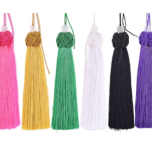 Puede incluir: Una colección de diez borlas coloridas, cada una con una parte superior anudada y una parte inferior con flecos. Las borlas son de varios colores, incluyendo negro, azul, rosa, amarillo, verde, blanco y morado. Cada borla mide unos 15 cm de largo.