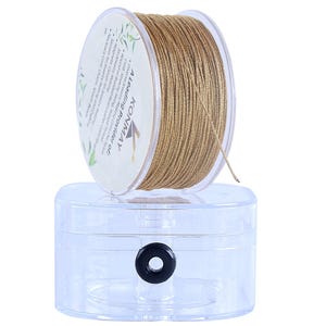 Könnte beinhalten: Eine Spule mit metallisch goldfarbenem Schmuckband, aufgewickelt auf eine durchsichtige Kunststoffrolle, mit dem Text KONMAY A Leading Provider of: Jewelry Making Cord, Waxed Thread, Necklace Cord, Chains, and more, auf einem durchsichtigen Kunststoffbehälter.
