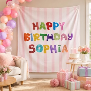 May include: A white fabric backdrop with vertical light pink stripes featuring the colorful text HAPPY BIRTHDAY SOPHIA in various patterns. The scene includes a cluster of pink and white balloons, a birthday cake, and wrapped gift boxes.