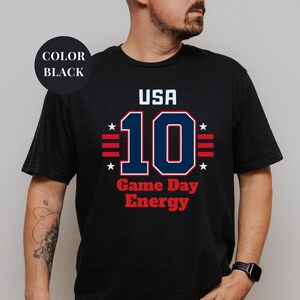 A man wearing a black t-shirt with the text "USA 10 Game Day Energy" printed on it.
