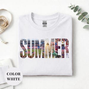 White Gildan t-shirt featuring a "SUMMER" photo collage graphic. The bold block letters are filled with USA soccer scenes, including a packed stadium, American flags, cheering fans, and a diving goalie. Patriotic sports apparel for World Cup 2026 supporters.