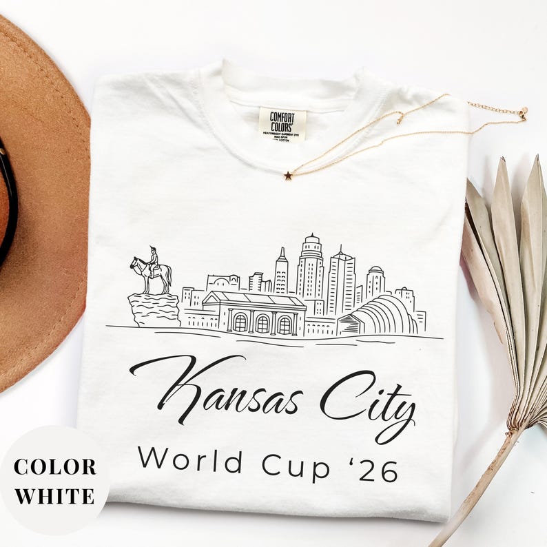 White Comfort Colors T-shirt featuring a minimalist black line art Kansas City skyline design, elegant Kansas City script lettering, and World Cup ’26 text, styled as a soccer travel souvenir shirt for Kansas City fans, football lovers, and 2026 World Cup city apparel.
