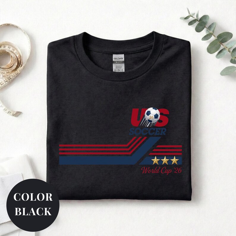 A black t-shirt with a graphic design featuring a soccer ball, stripes, and stars, along with the text "US SOCCER" and "World Cup 26".