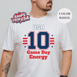 A man wearing a white t-shirt with a graphic design featuring the text "USA 10 Game Day Energy" and the number 10.
