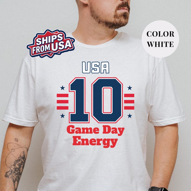 A man wearing a white t-shirt with a graphic design featuring the text "USA 10 Game Day Energy" and the number 10.