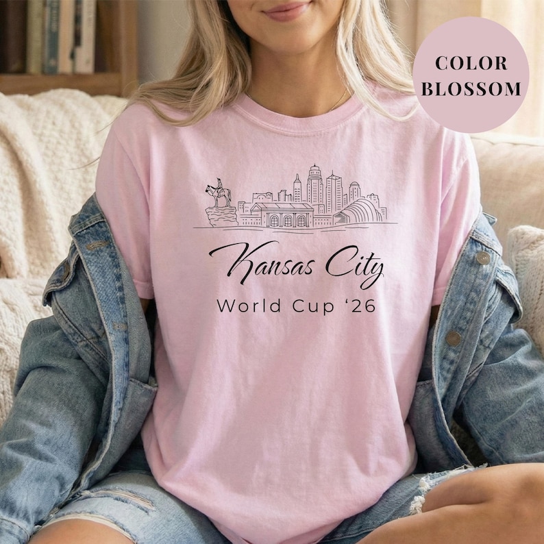 Blossom Comfort Colors T-shirt featuring a minimalist black line art Kansas City skyline design, elegant Kansas City script lettering, and World Cup ’26 text, styled as a soccer travel souvenir shirt for Kansas City fans, football lovers, and 2026 World Cup city apparel.